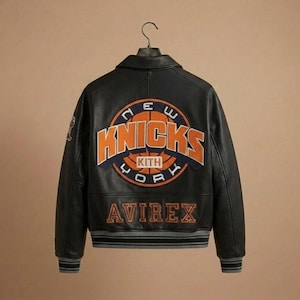 Puede incluir: Una chaqueta universitaria de cuero negro con un gran logotipo de baloncesto de los New York Knicks bordado en la espalda, que incluye el texto KITH en el centro. La palabra AVIREX est&aacute; bordada debajo en naranja y tiene pu&ntilde;os acanalados a rayas.
