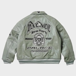 May include: A light green leather jacket with a classic collar and ribbed cuffs. The back features the text "PALACE New York" in a stylized font, along with additional text and emblems. The jacket has a white stripe detail.