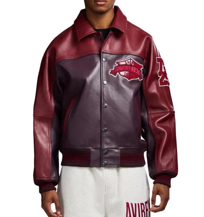 Puede incluir: Chaqueta de cuero burdeos y burdeos oscuro con cierre de botones, cuello y pu&ntilde;os y dobladillo acanalados. La chaqueta presenta un parche con el texto "AVIREX" y el n&uacute;mero "74" en la manga.