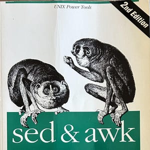 May include: A softcover technical book titled sed & awk, 2nd Edition, from the O'Reilly UNIX Power Tools series. The white cover features a black and white illustration of two primates perched above a green rectangular block containing the title text.