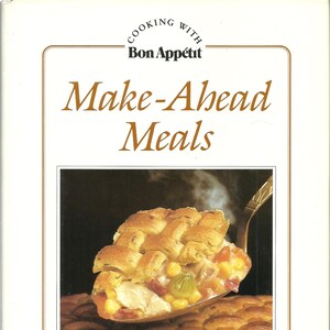 May include: A cookbook cover with the title "Make-Ahead Meals" by Bon Appétit. The image features a close-up of a savory pie with a woven crust, served on a silver spoon. The pie filling includes corn, chicken, and other vegetables.