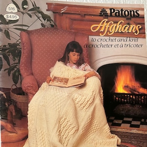 May include: A book cover featuring a young person reading under a cream-colored crocheted afghan. The book cover has the title "Patons Afghans" and the text "to crochet and knit". The cover also has the text "Patons Canadiana Beehive ASTRA".