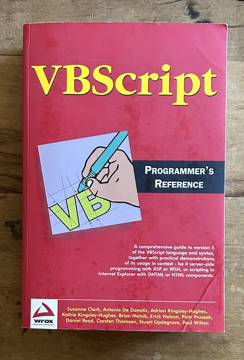 May include: A red VBScript Programmer's Reference book with yellow text. The cover features a graphic of a hand holding a blue pen over the letters VB on a grid. It includes the subtitle A comprehensive guide to version 5 of the VBScript language.