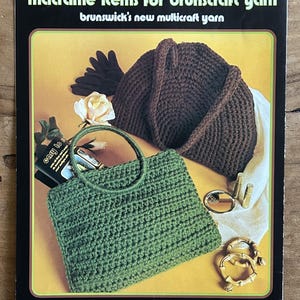 May include: A vintage craft pattern booklet titled crochet, stitchery and macramé items for brunscraft yarn, featuring a dark brown crocheted handbag and a green crocheted handbag with round handles, alongside a rose, gloves, and gold accessories.