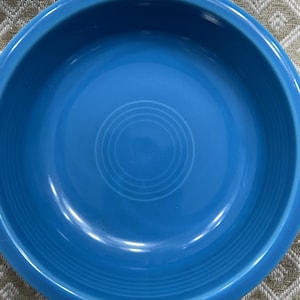 May include: A vibrant, solid turquoise blue ceramic bowl. The bowl has a rounded shape with a slightly raised rim and concentric circles in the center. The bowl is likely for serving food.