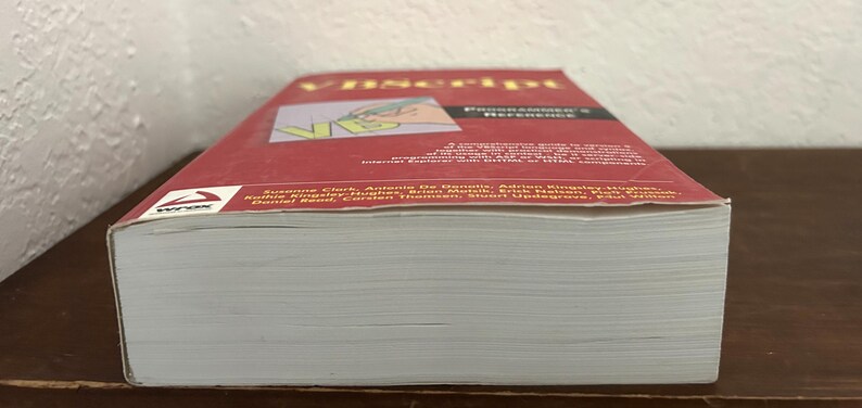 May include: A thick paperback book titled VBScript Programmer's Reference with a red cover. The cover features the text VBScript, a graphic of a hand writing with a pen, and a list of authors including Suzanne Clark and Antonio De Donatis.