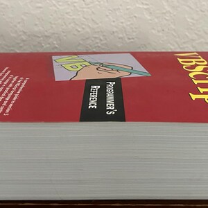 May include: A thick paperback book titled VBScript Programmer's Reference with a red cover. The cover features a graphic of a hand holding a green pen over the letters VB. The text is printed in yellow and white against a red and black background.