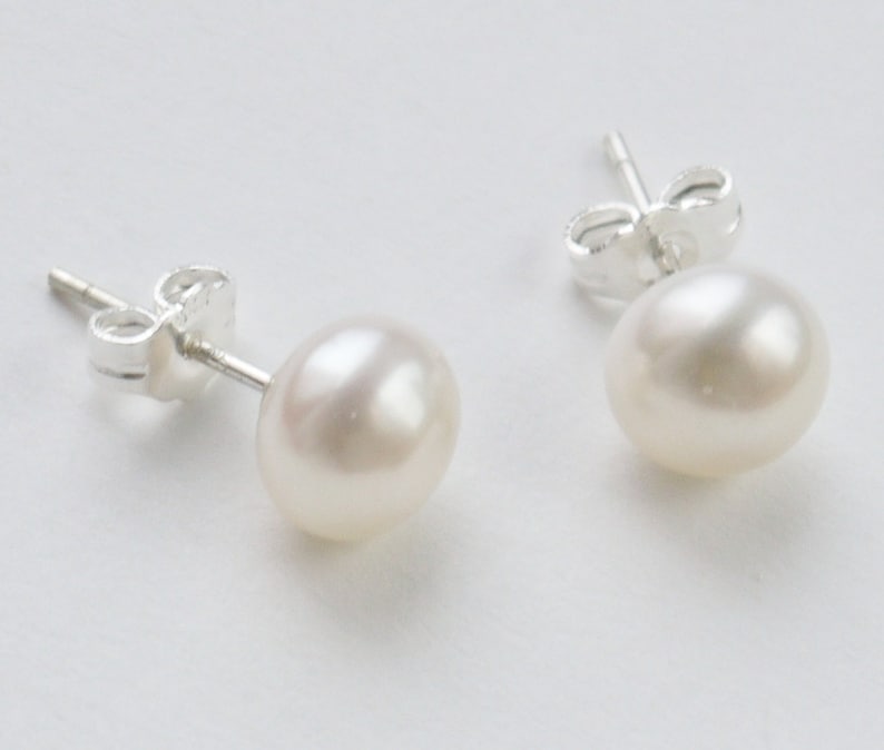 May include: A pair of silver stud earrings with white pearl accents.