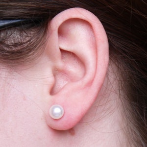 May include: A close-up of a person's ear with a small, white pearl earring.
