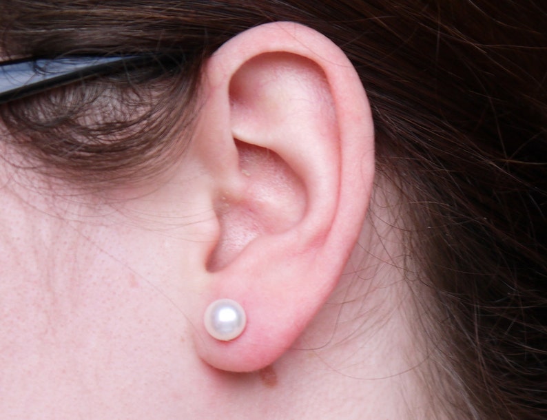 May include: A close-up of a person's ear with a small, white pearl earring.