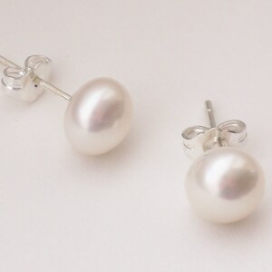 May include: A pair of pearl stud earrings with silver posts and backs. The pearls are white and round.