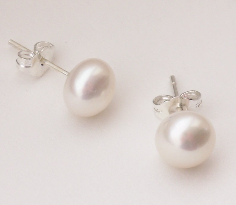 May include: A pair of pearl stud earrings with silver posts and backs. The pearls are white and round.