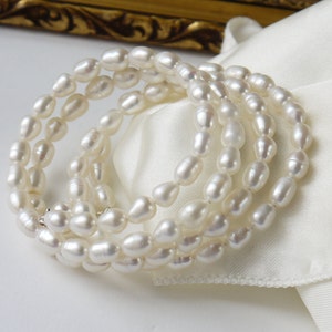May include: A set of four white pearl bracelets, each with a different length. The pearls are oval shaped and have a smooth, glossy finish.