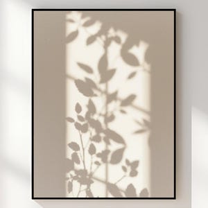 Puede incluir: Una impresión enmarcada con un fondo beige, que muestra la sombra de hojas y ramas en gris oscuro. La impresión está encerrada en un marco negro. El texto "RSM Digital Prints" es visible en la parte inferior de la imagen.
