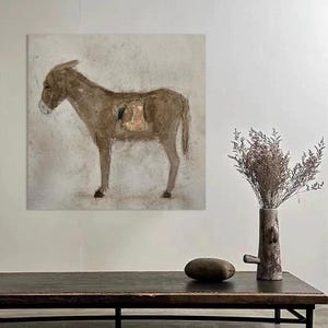 Puede incluir: Una pintura de un burro marrón sobre un lienzo cuadrado. El burro se representa de perfil, con una representación detallada de su forma y un aspecto texturizado. La obra de arte se exhibe en una pared blanca, con una mesa de madera oscura y un jarrón decorativo en primer plano.