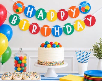 May include: A birthday party set featuring a colorful banner with the text HAPPY BIRTHDAY, a white frosted cake topped with multi-colored spheres, a glass jar filled with round candies, white frosted cookies with sprinkles, and blue striped straws.