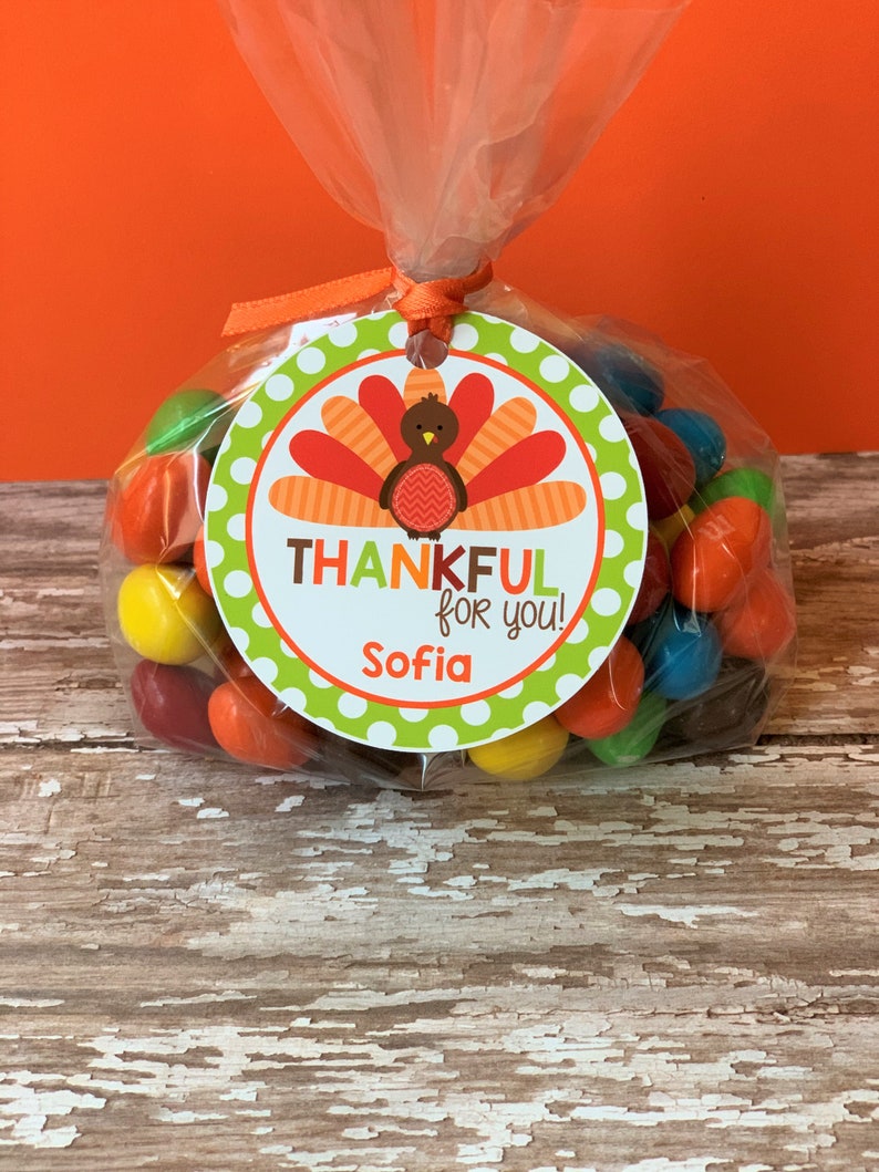 Op de afbeelding: Een doorzichtige plastic zak gevuld met kleurrijke snoepjes, vastgebonden met een groen-wit geblokt lint. Een rond label met een kalkoenillustratie en de tekst "THANKFUL for you! Sofia" is aan de zak bevestigd.