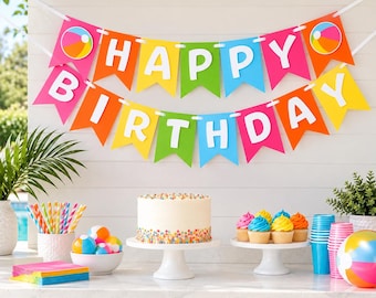 May include: A colorful Happy Birthday banner with beach ball accents hangs above a table featuring a white cake with sprinkles, cupcakes, a bowl of small beach balls, striped straws, and a large beach ball on a white surface.