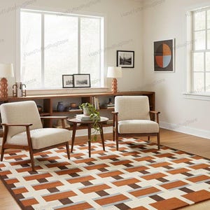 Op de afbeelding: Een woonkamer met een geometrisch patroon tapijt in bruin, oranje, grijs en crème. Twee fauteuils met lichtgekleurde bekleding en houten frames staan op het tapijt. Een kleine ronde tafel en een houten plank met decoratie maken de kamer compleet.