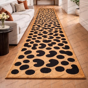 Puede incluir: Una alfombra larga y rectangular con un fondo beige y grandes manchas negras irregulares. La alfombra, que recuerda a un estampado de leopardo, está colocada sobre un suelo de madera, probablemente en un pasillo. El diseño es adecuado para espacios largos.