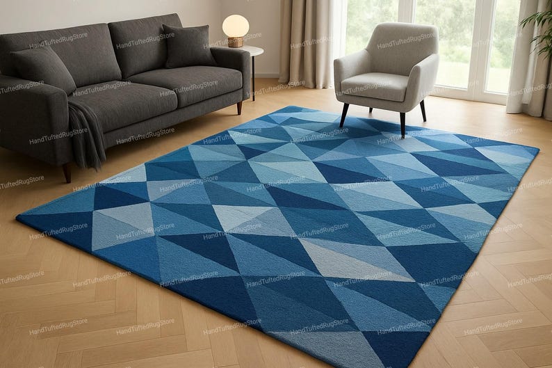Puede incluir: Una alfombra rectangular grande con un patr&oacute;n geom&eacute;trico de tri&aacute;ngulos azules y celeste. La alfombra est&aacute; colocada sobre un suelo de madera, con un sof&aacute; gris, un sill&oacute;n y una peque&ntilde;a mesa auxiliar con una l&aacute;mpara en el fondo. Las dimensiones de la alfombra no son visibles.