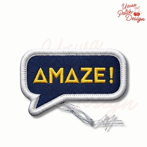 May include: Embroidered patch in a speech bubble shape. The patch features the word "AMAZE!" in yellow, embroidered on a navy blue background. The border is white, with loose threads at the bottom. The patch is a design by Uzura Patch Design.