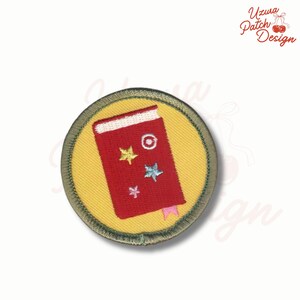 May include: Round embroidered patch featuring a red book with a white spine, a pink bookmark, and three stars. The book is on a yellow background, surrounded by a green border. The text "Uzura Patch Design" is in the upper right corner.