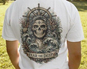 May include: White t-shirt featuring a detailed graphic on the back. The design includes a skull with flowing hair, a ship's wheel, and ocean waves. The text "FEAR THE DEEP" is displayed on a banner below the skull. The shirt is worn by a person.