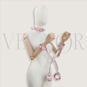 May include: Pink leather collar, wrist cuffs, and ankle cuffs set with silver-tone hardware. The set includes connecting straps and a small pouch. The items are displayed on a mannequin.