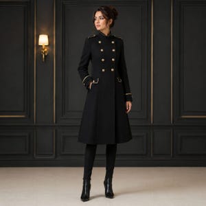 May include: A black knee-length coat featuring a high collar, double-breasted front with gold-toned buttons, structured shoulders with epaulets, and long sleeves with gold-toned trim at the cuffs. The coat is paired with black trousers and black boots.