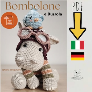 May include: A crochet amigurumi hippo wearing a dark brown aviator hat with goggles and a small light blue bird on its head. The hippo has a light gray body with striped arms in green, white, and peach. Text includes Bombolone e Bussola, PDF, and @ILPICCOLOLAB.