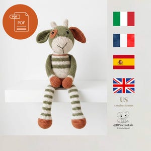 Può includere: Una bambola giraffa all'uncinetto fatta a mano con corpo a righe verdi e bianche, orecchie marroni e piedi arancioni. La bambola è seduta su una mensola bianca. L'immagine include anche un'icona PDF.