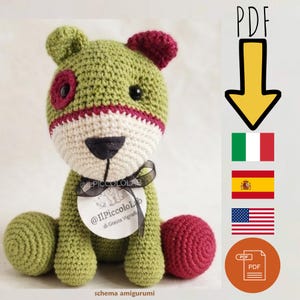 Puede incluir: Un juguete amigurumi de ganchillo en verde oliva, crema y rosa oscuro. Presenta una nariz negra, ojos negros y una cinta negra alrededor del cuello que sostiene una etiqueta circular con el texto @IlPiccoloLab di Grazia Vignoli. Incluye icono PDF.