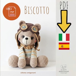 Può includere: Un orsacchiotto all'uncinetto con un cappello da aviatore marrone con dettagli blu. L'orso è seduto con le braccia e le gambe distese. La parola "Biscotto" è sopra l'orso. Include un'icona PDF e le bandiere italiana e spagnola.