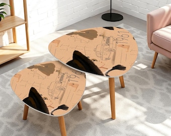 May include: A set of two nesting tables with a light tan surface featuring a black line drawing of a vintage car and the text 1961. Each table has three light brown wooden legs and a rounded triangular top with a smooth finish.