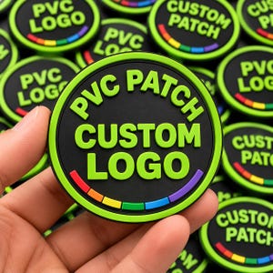 May include: A circular black PVC patch featuring raised lime green text that reads PVC PATCH CUSTOM LOGO. The border is lime green with a segmented rainbow-colored arc at the bottom. The patch has a matte finish and a distinct embossed texture.