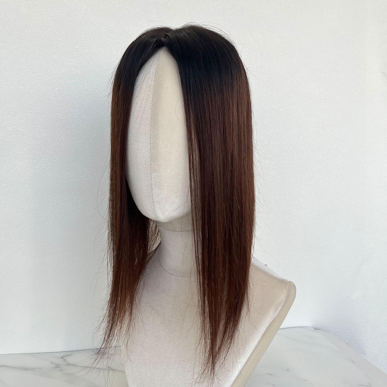 以下が含まれることがあります： マネキンの頭に展示されている茶色と黒のヘアートッパー。髪はストレートで肩まで届きます。ヘアートッパーは、濃い茶色の根元から明るい茶色にフェードしています。