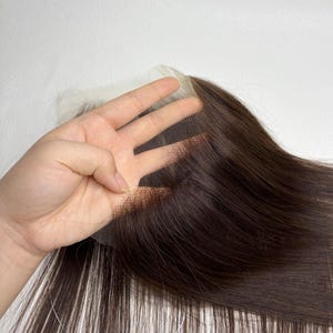 May include: A dark brown lace front wig closure with long, straight hair. The lace is a fine mesh, and the hair is a rich, natural color. The wig is designed to be sewn or glued onto the hairline for a seamless look.