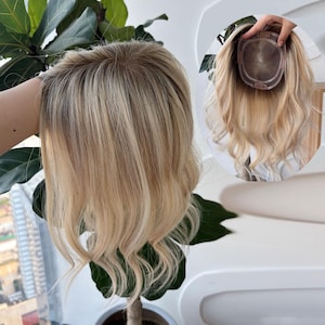以下が含まれることがあります： ダークな根元と柔らかなウェーブが特徴のブロンドヘアのヘアトッパー。円形のベースには透明なモノフィラメントのトップが付いており、周囲には頭部にしっかりと固定するための小さなクリップが取り付けられています。2つの角度から撮影されています。