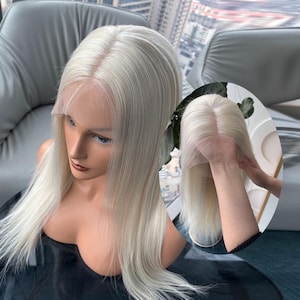 May include: A platinum blonde wig with long, straight hair. The wig is styled with a natural-looking part and lace front. The wig is displayed on a mannequin head with a black top.