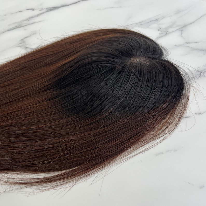 以下が含まれることがあります： 長くてストレートな髪の毛の、濃い茶色と黒のヘアートッパー。ヘアピースは、濃い根元から明るい茶色にフェードするデザインです。ヘアピースは、自然な髪の毛にボリュームと長さを加えるように設計されています。