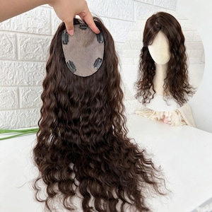 May include: A dark brown hair topper featuring long, wavy strands and a monofilament base with four integrated pressure-sensitive clips for secure attachment. The hairpiece is shown from the underside and displayed on a mannequin head.
