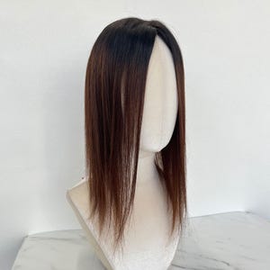 以下が含まれることがあります： マネキンの頭に展示された茶色と黒のヘアートッパー。髪はストレートで肩まで届きます。ヘアートッパーは、根元に濃い茶色から黒へのグラデーション効果があります。