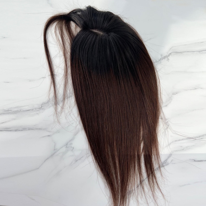 以下が含まれることがあります： 黒い根元の部分がある、濃い茶色のヘアトッパー。ヘアピースは長くまっすぐな毛束と小さな円形のベースを持っています。ヘアピースは、自然な髪にボリュームと長さを加えるように設計されています。