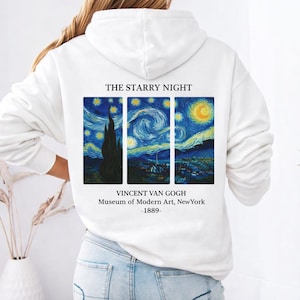 Puede incluir: Sudadera con capucha blanca con un estampado de "La noche estrellada" de Vincent van Gogh. La obra de arte se muestra en tres paneles, con el texto "THE STARRY NIGHT" arriba e información del artista y el museo abajo.