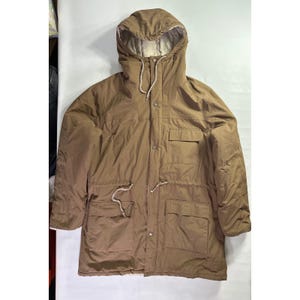 Pode incluir: Parka marrom com capuz e cordão na cintura. O casaco tem dois bolsos frontais grandes e dois bolsos no peito menores. O forro interior do capuz é de cor creme claro. O casaco é abotoado na frente.