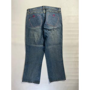 May include: Light blue denim jeans with pink stitching around the back pockets. The pockets have a unique heart-shaped design. The jeans have a classic five-pocket design and a straight leg cut.