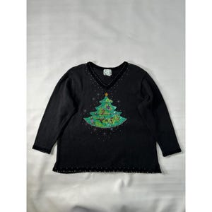 May include: Black long-sleeved sweater with a V-neck and a Christmas tree design. The tree is green with sequins and a gold star. The sweater has a beaded trim along the neckline, cuffs, and hem.