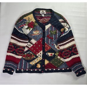 Puede incluir: Cárdigan vintage con botones y diseño patchwork. El suéter presenta varios patrones y detalles bordados, incluyendo rosas, tazas de té y formas geométricas. La paleta de colores incluye azul marino, rojo, crema y verde.