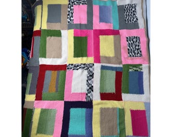 May include: A colorful, handmade knitted blanket with a patchwork design. The blanket features a variety of rectangular blocks in shades of pink, green, blue, yellow, gray, and black and white patterns. The blanket is made of soft yarn and is perfect for snuggling.
